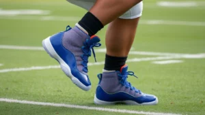 Professional football player in defensive stance wearing blue Air Jordan 11s, mid-cut athletic shoe with patent leather details, executing sharp lateral cutting movement on grass field, dynamic action shot emphasizing agility and foot positioning
