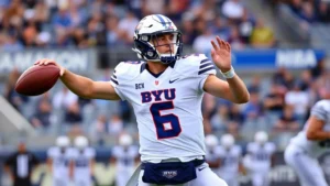 College football quarterback in mid-throw, wearing BYU uniform, stadium background, action shot capturing athletic form and concentration during game