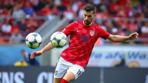 Professional footballer in Croatian red checkered jersey executing precise passing technique during international match, stadium background, dynamic action shot