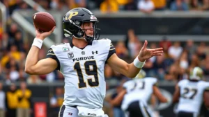 Professional college football quarterback in Purdue uniform throwing football mid-spiral during intense game action with stadium background, showing athletic form and concentration
