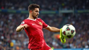 Professional male soccer player in red jersey executing perfect pass during international match with stadium crowd in background, dynamic action shot capturing ball control and technical skill