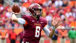 College football quarterback in Virginia Tech maroon jersey throwing football mid-game, stadium background blurred, dynamic action shot, athletic form, professional sports photography