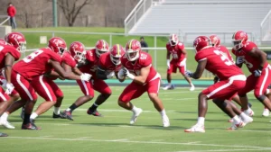 College football team in defensive stance during practice, players in red uniforms executing tackling drills on field, intense focus and athletic form, afternoon daylight, no text or labels