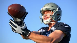 Professional football player wearing gloves performing one-handed catching drill during outdoor practice with clear blue sky, focused expression, athletic form