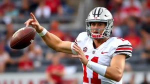 Professional football quarterback in Ohio State uniform throwing football during intense practice drill, sweat visible, focused expression, stadium background blurred